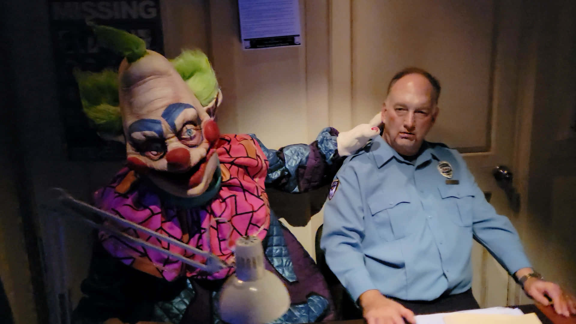 A Clown Dressed As A Police Officer Sits Next To A Desk Background