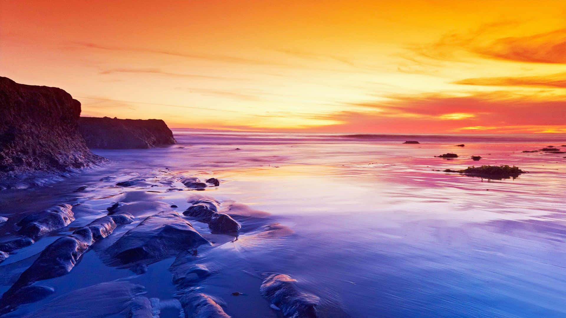 A Colorful Sunset Over The Ocean And Rocks Background