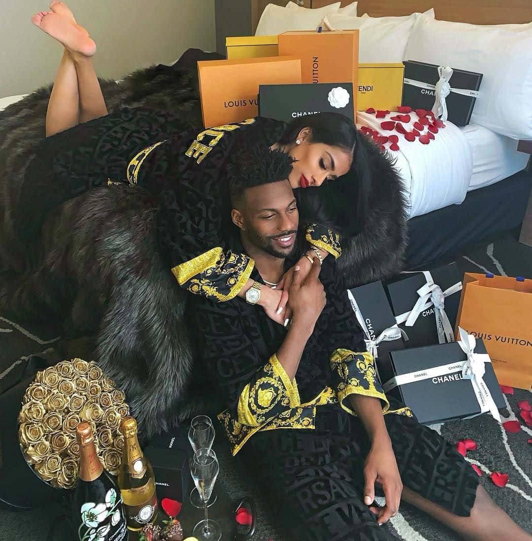 A Couple Laying On A Bed With Gifts On The Bed Background