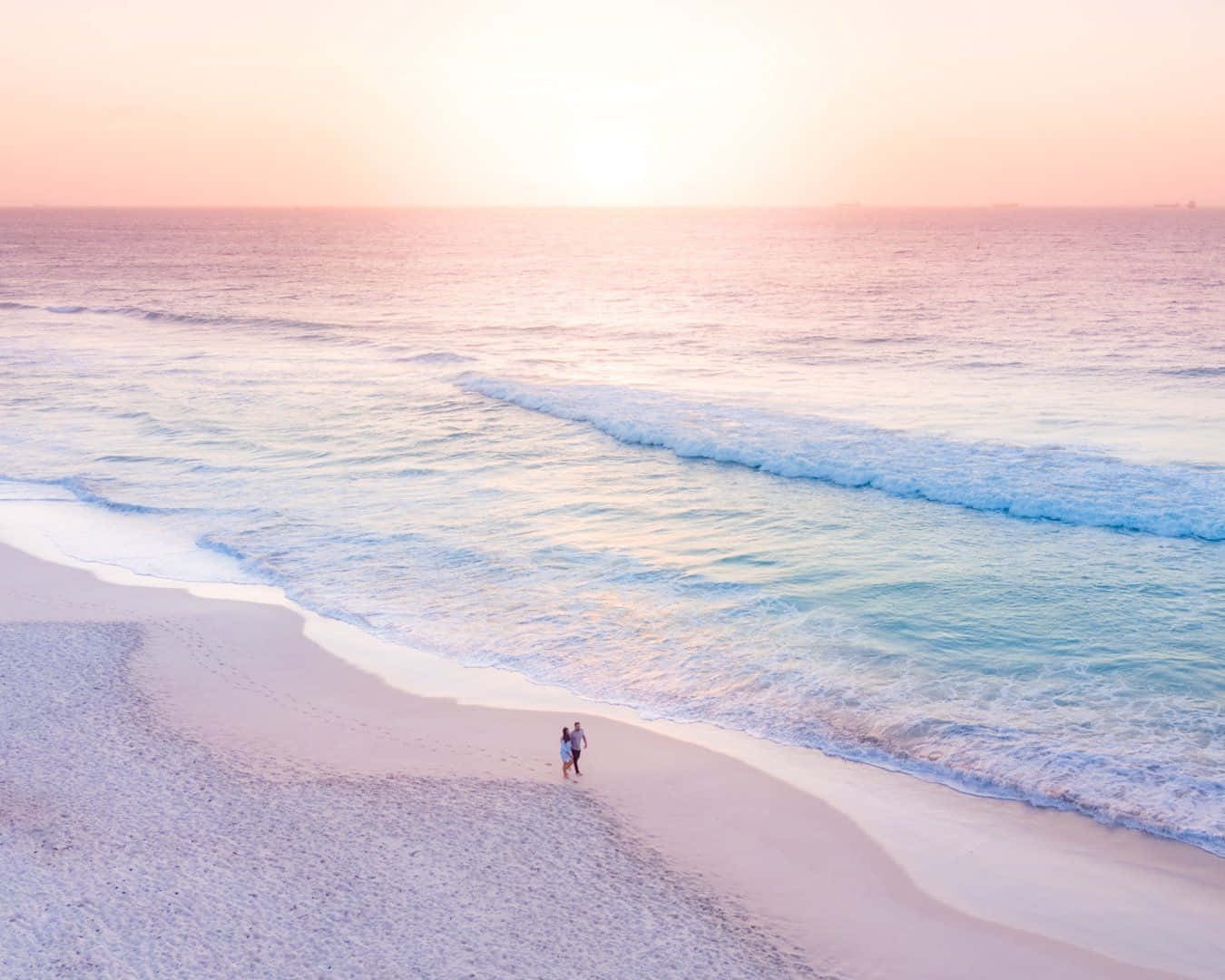 A Couple Walking On The Beach At Sunset Background