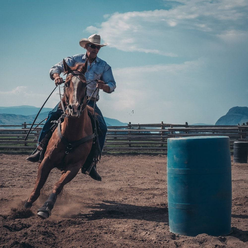 A Cowboy Riding A Horse In A Barrel Race Background