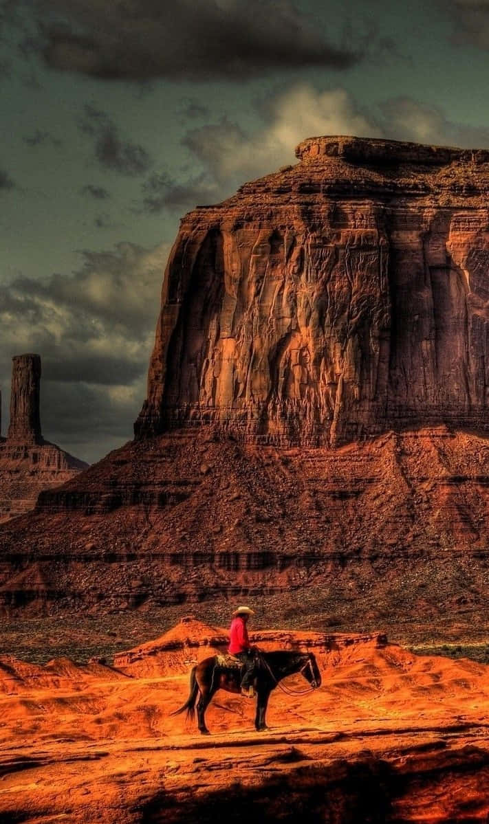 A Cowboy Riding A Horse In Monument Valley Background