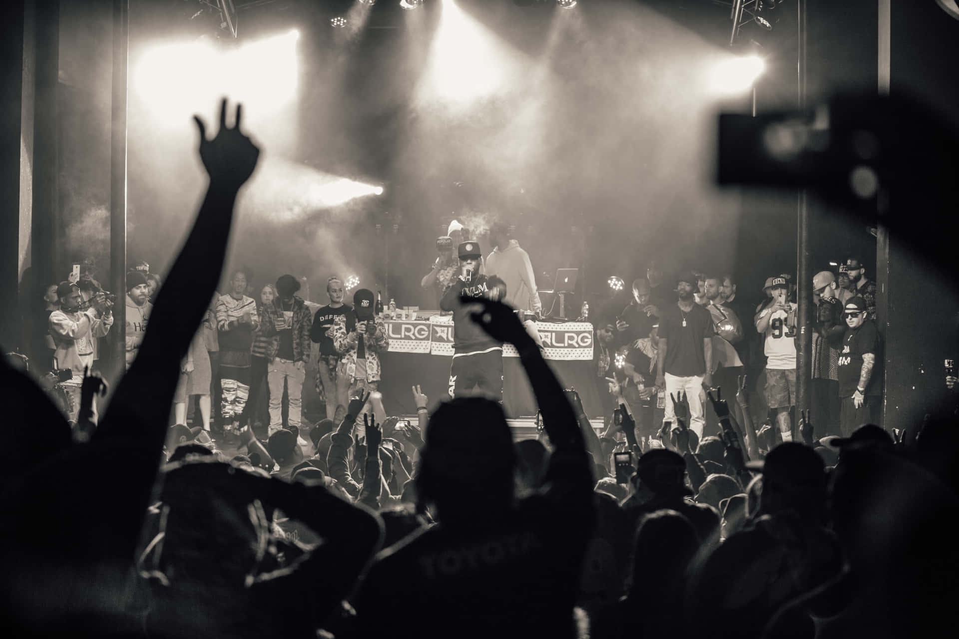 A Crowd Of People At A Concert With Their Hands Up Background