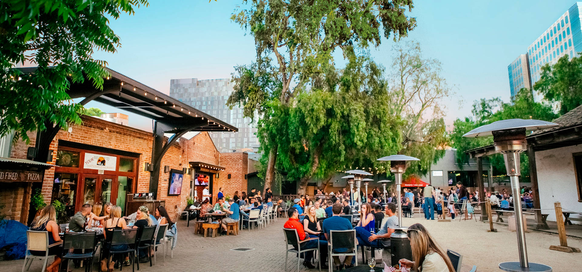 A Crowd Of People Sitting At Tables In A Courtyard