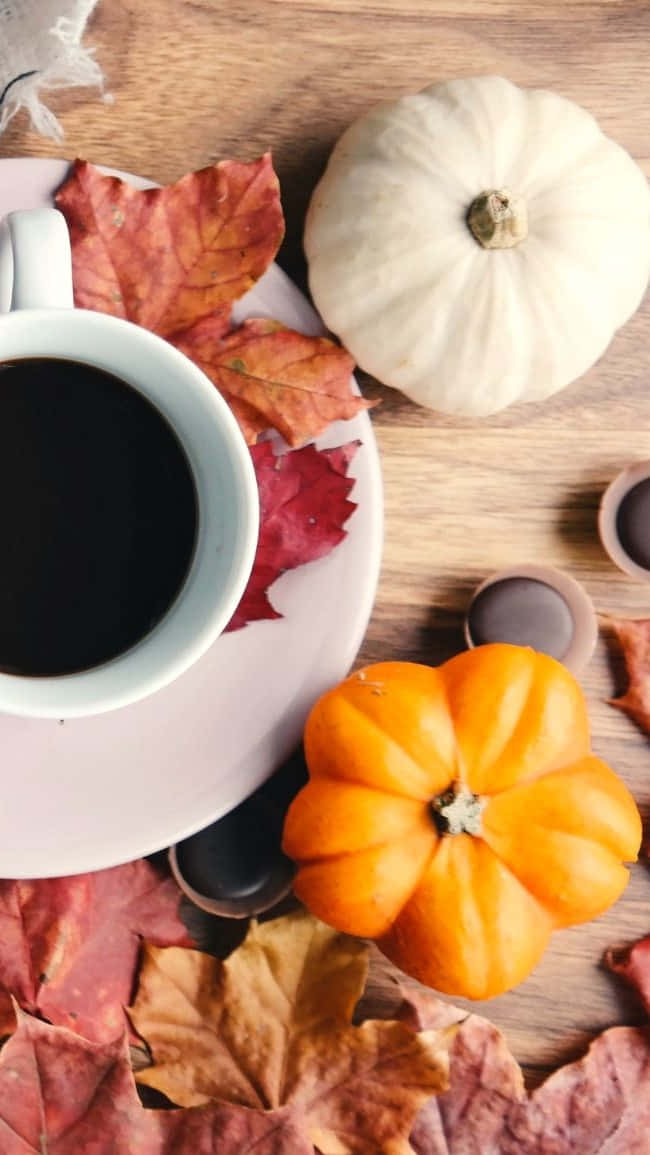 A Cup Of Coffee With Pumpkins And Leaves On A Wooden Table Background