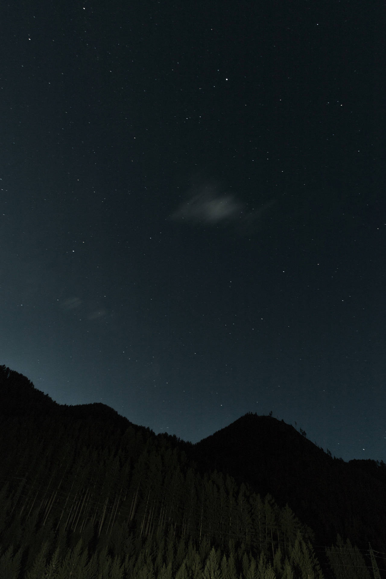 A Dimly Lit, Star-filled Sky Above A Stunning Mountain Silhouette.