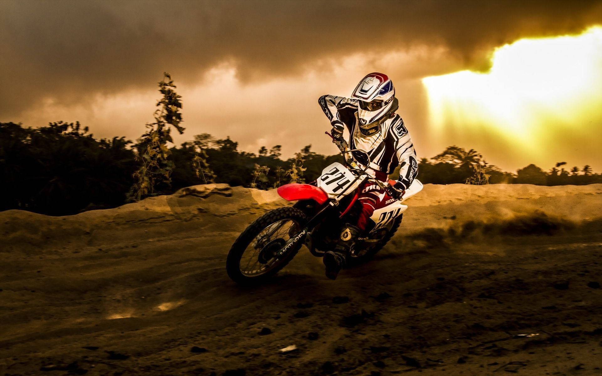 A Dirt Bike Rider Is Riding His Bike Through A Dirt Field Background