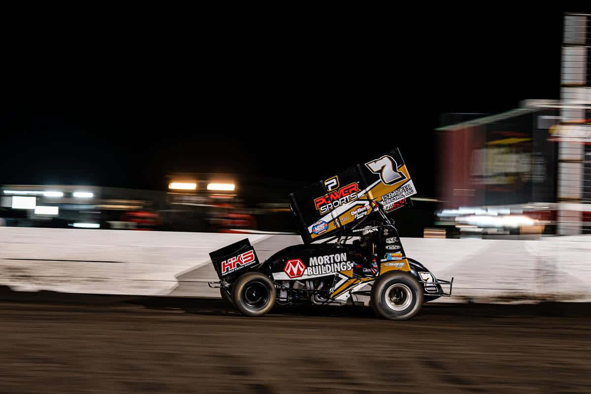 A Dirt Track Racer Driving At Night Background