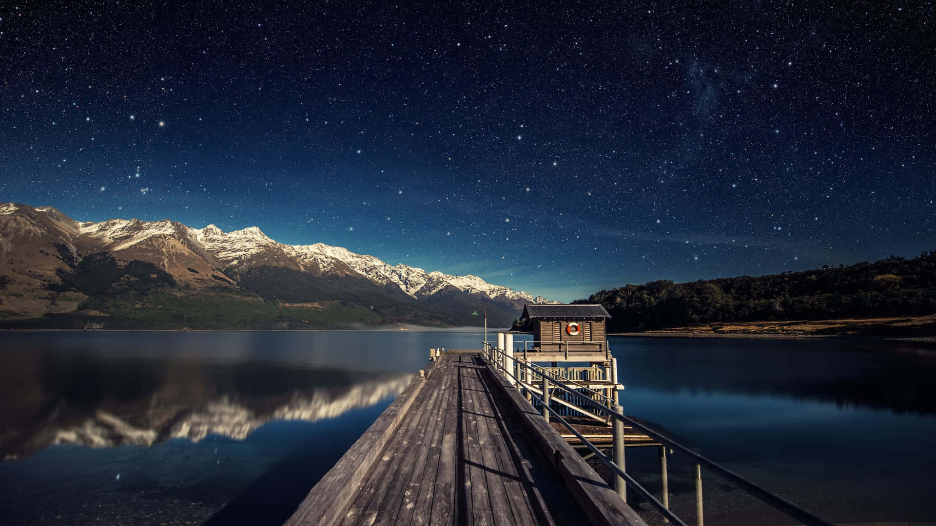A Dock With A Starry Sky And Mountains Background