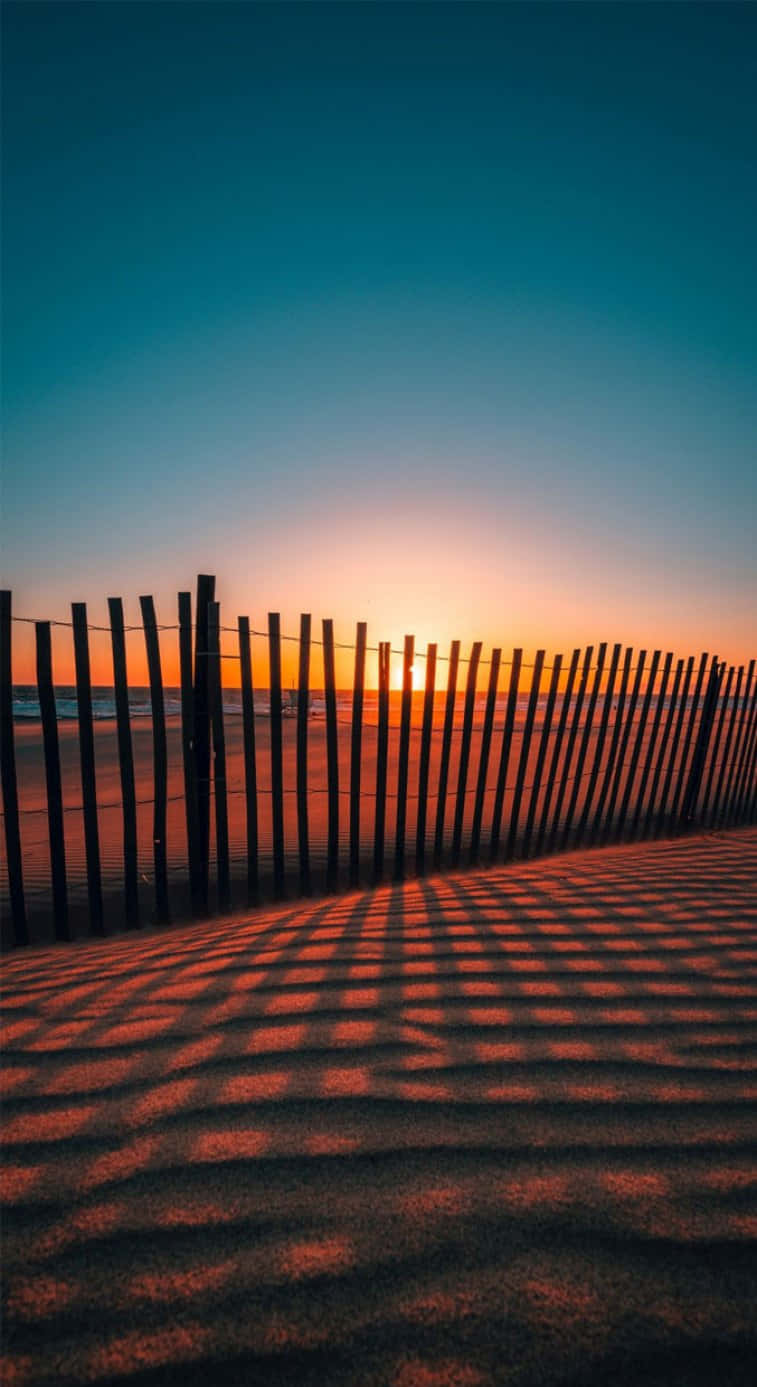 A Fence In The Sand At Sunset Background