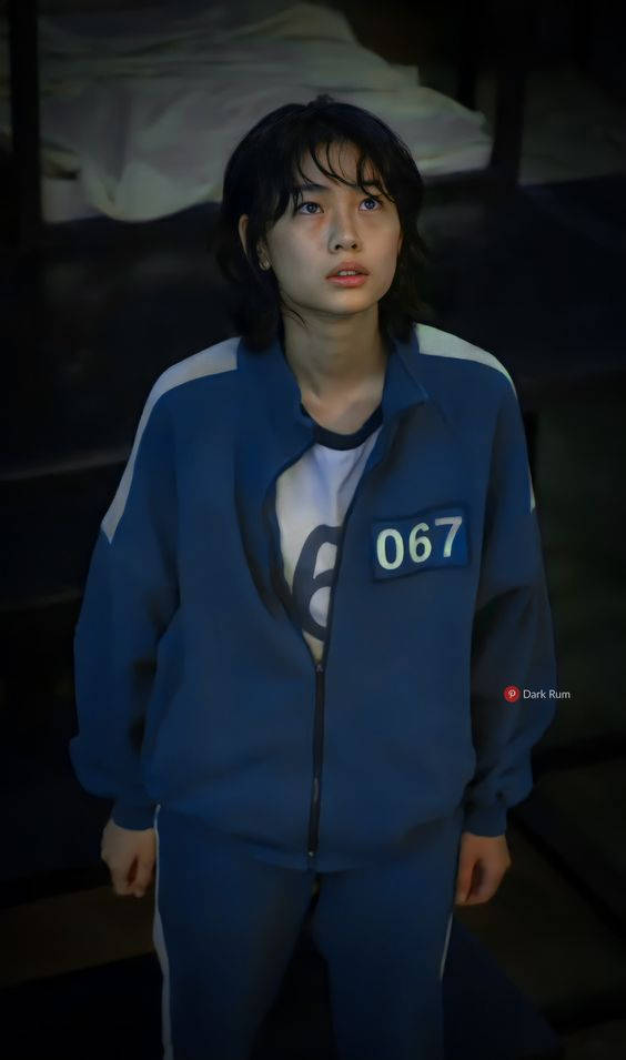 A Girl In A Blue Jacket Standing In Front Of A Bed Background