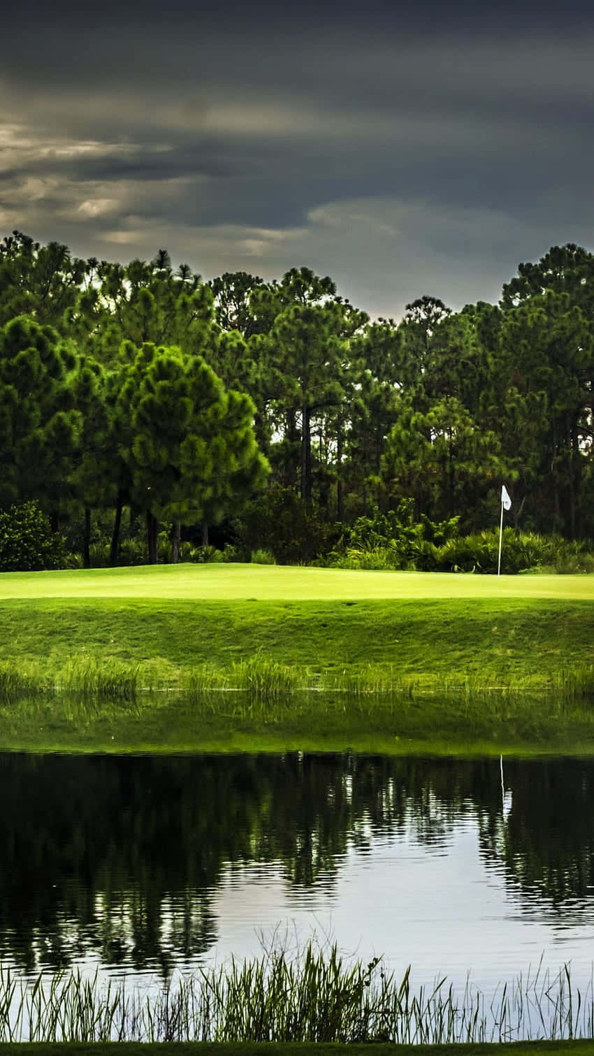 A Golf Course With A Pond And Trees Background