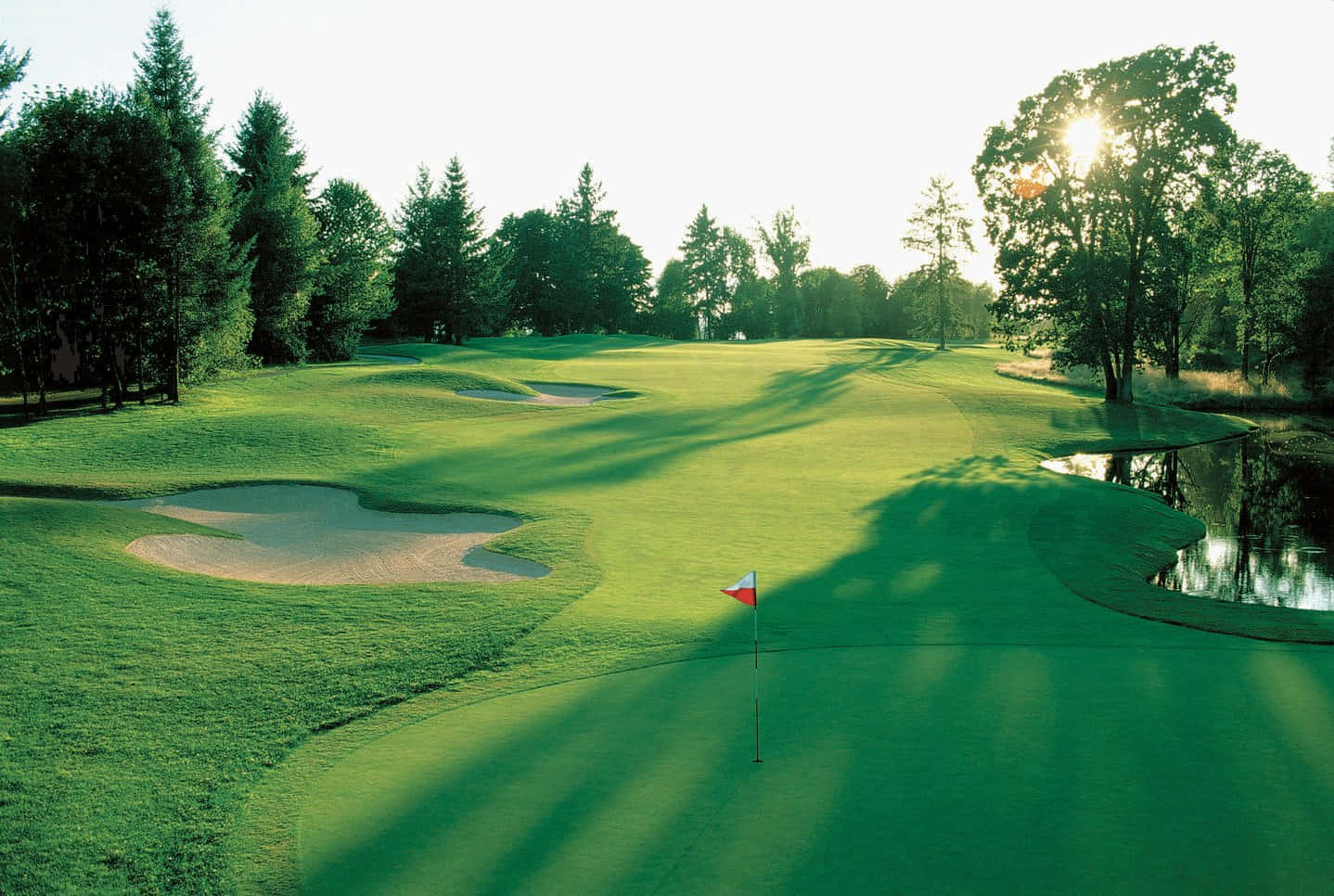 A Golf Course With A Pond And Trees Background