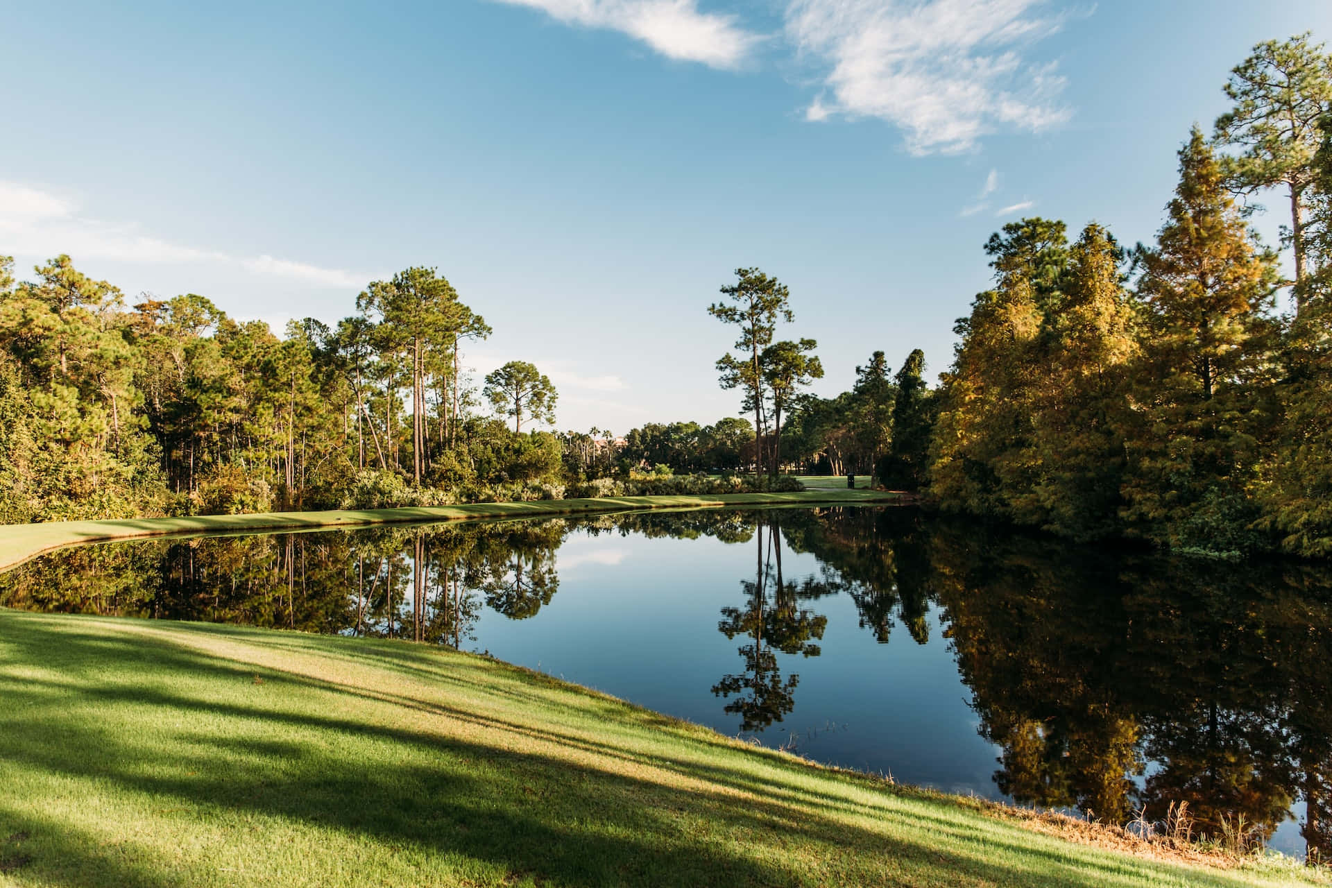 A Golf Course With Trees And A Pond Background