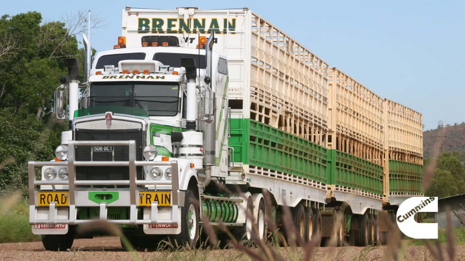 A Green And White Truck Driving Down A Dirt Road Background