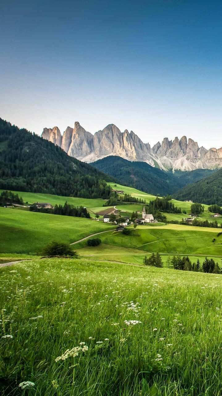 A Green Field With Mountains In The Background Background