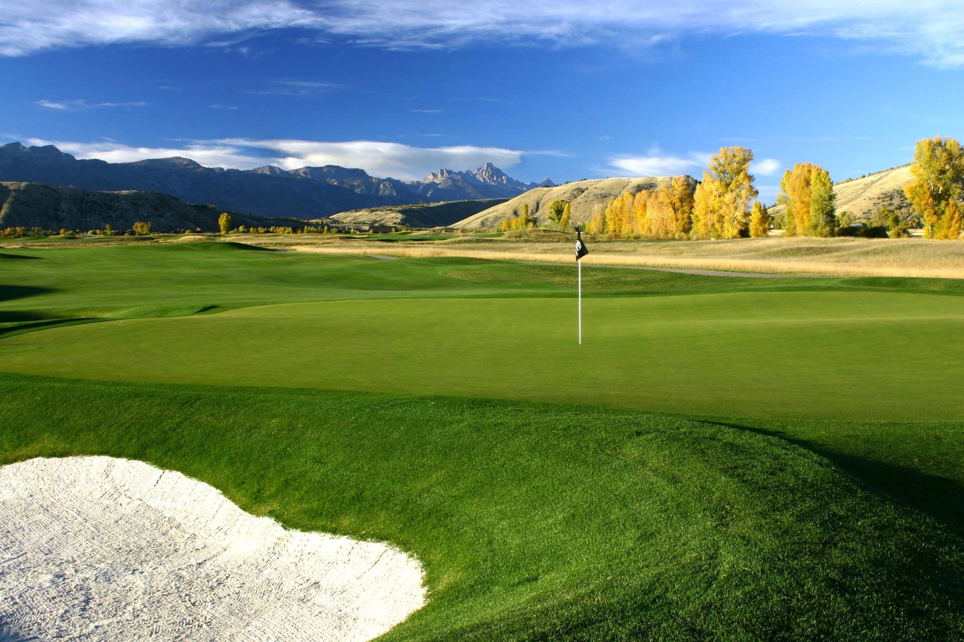 A Green Golf Course With Mountains In The Background Background