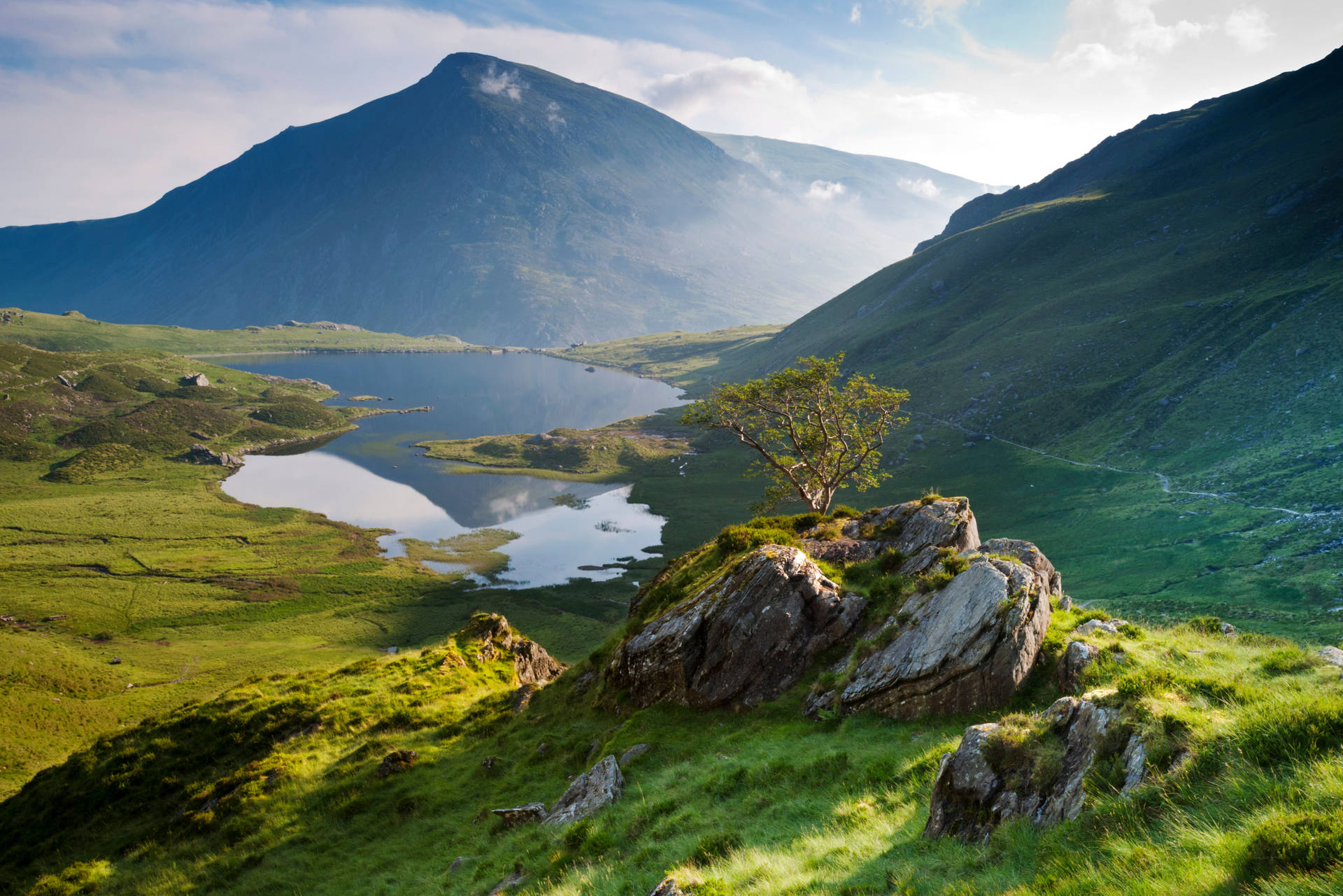 A Green Grassy Hillside With A Lake Background