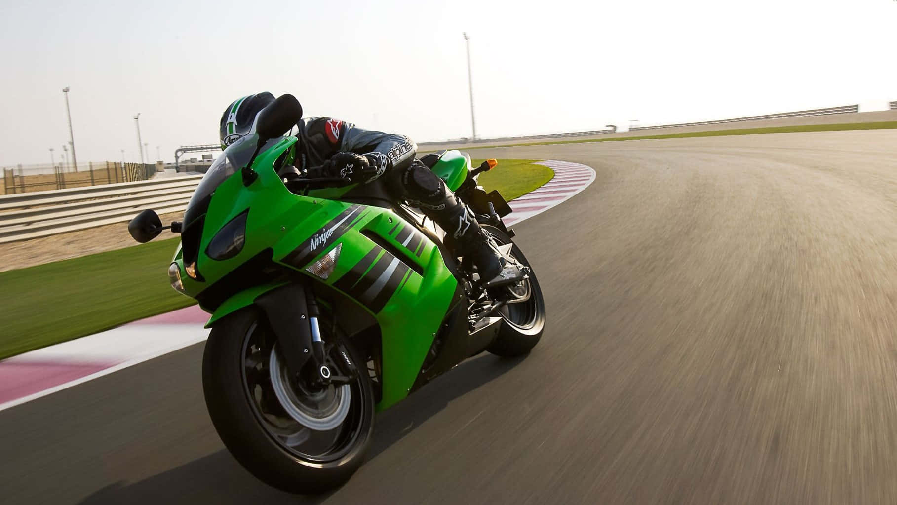 A Green Motorcycle Is Racing Down A Track Background