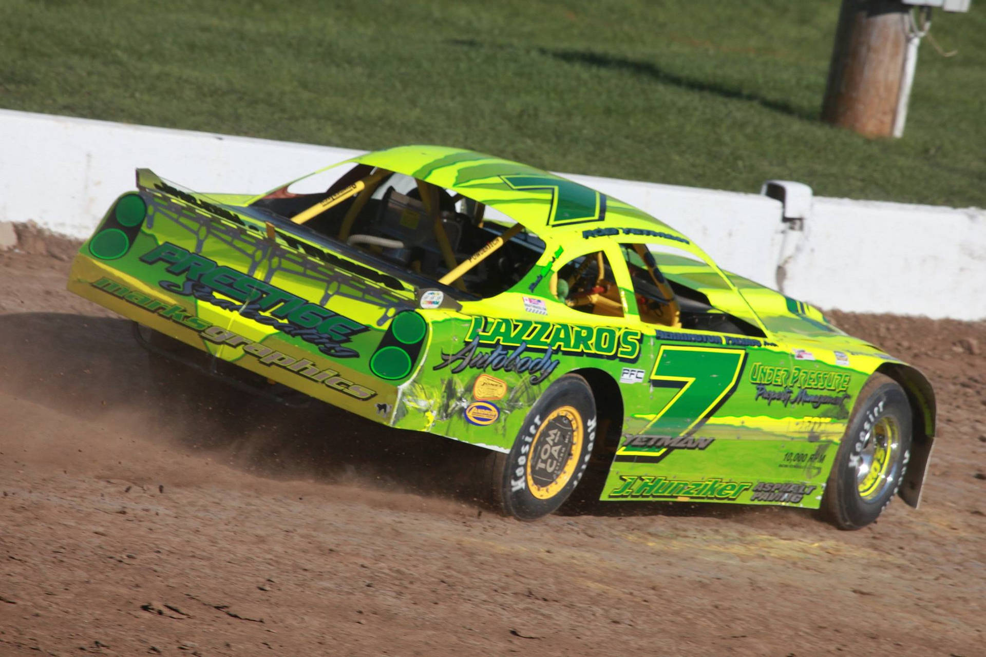 A Green Race Car Driving On A Dirt Track Background