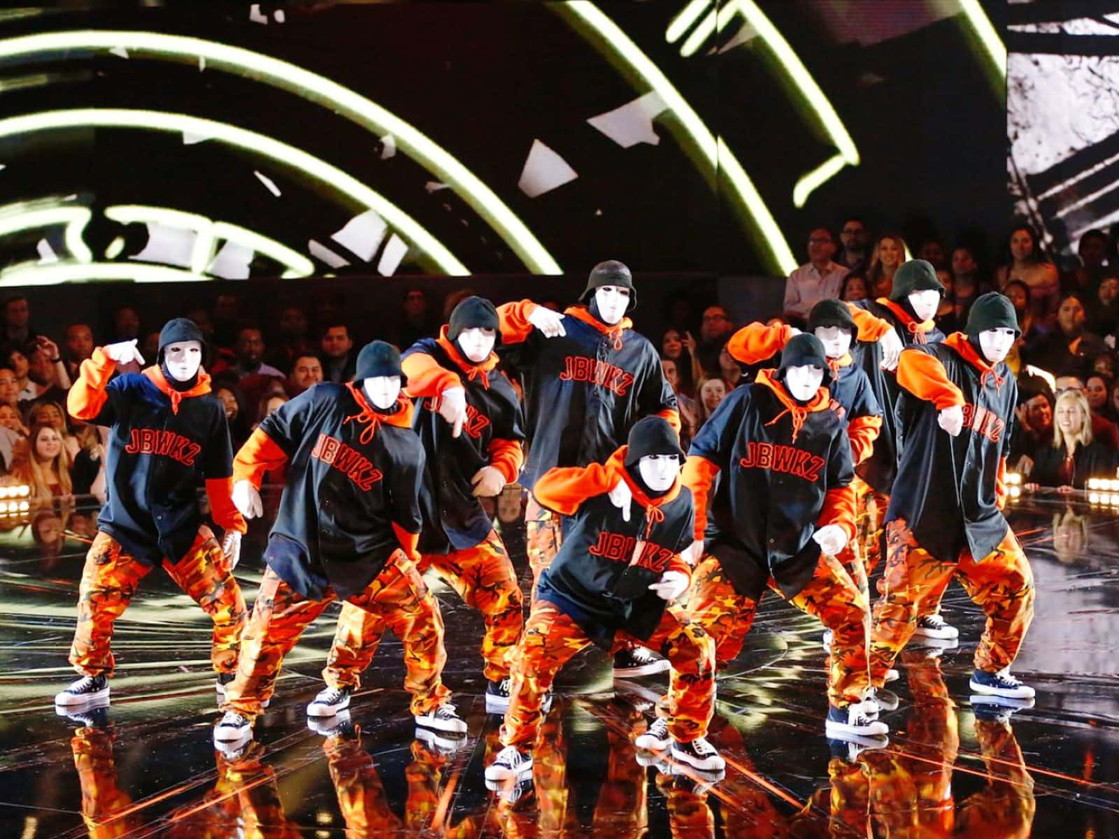 A Group Of Dancers In Orange And Black Outfits Background