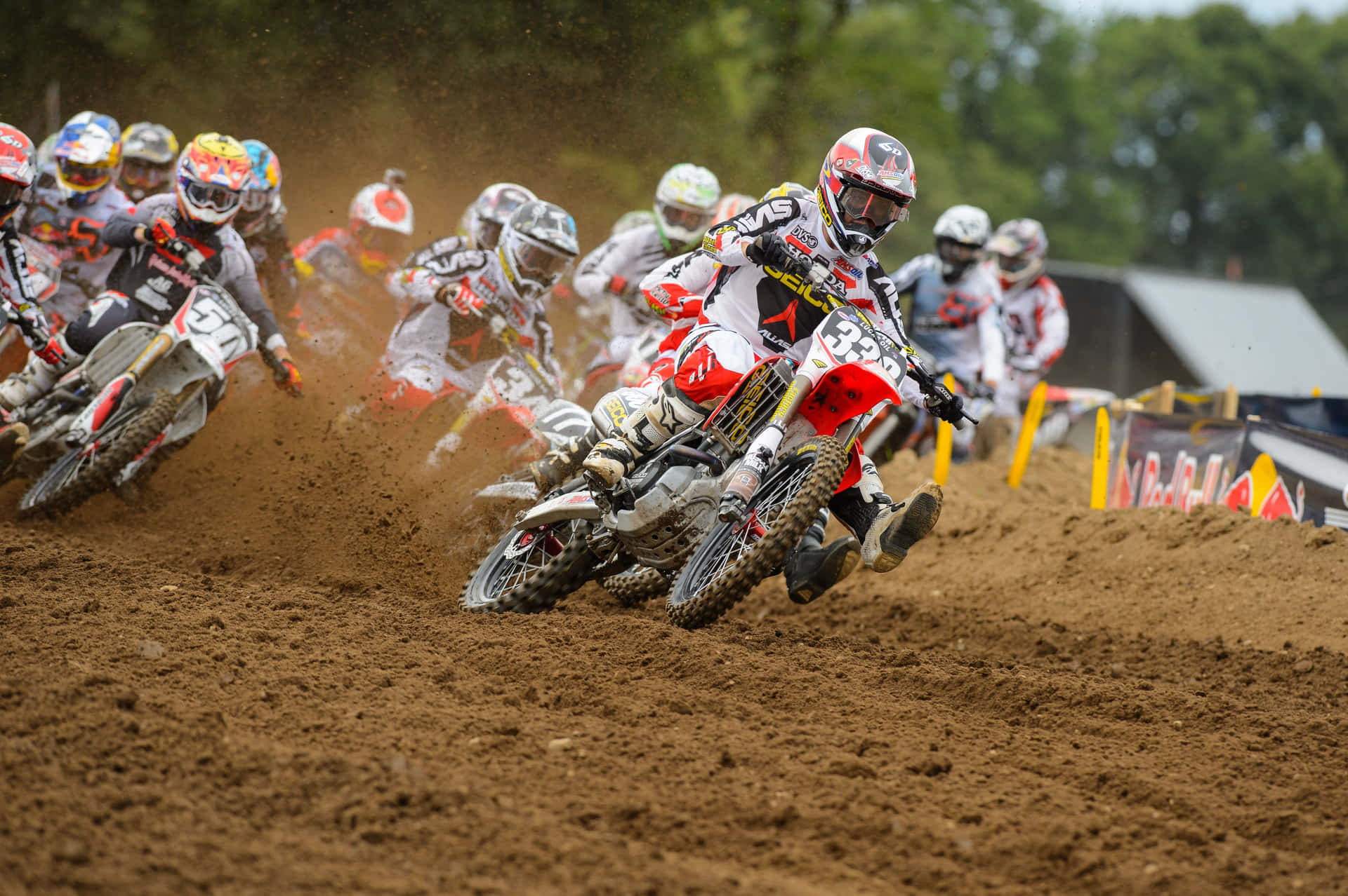 A Group Of Dirt Bikers Racing On A Dirt Track Background