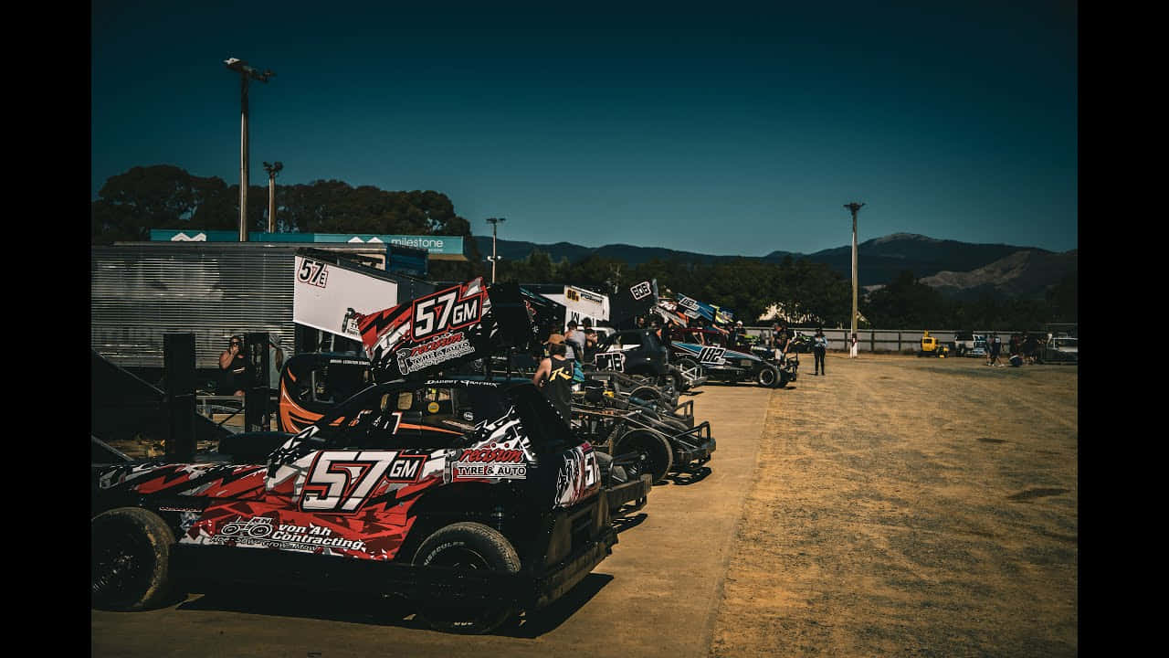 A Group Of Dirt Track Cars Parked In A Dirt Lot Background