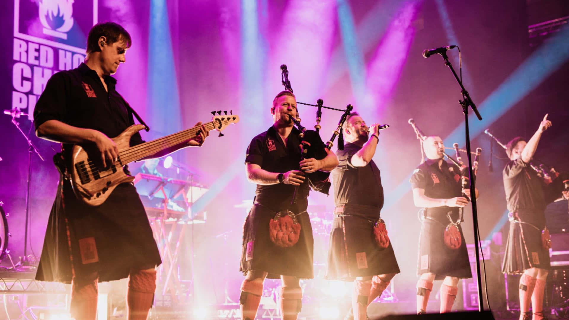 A Group Of Men In Kilts On Stage Background