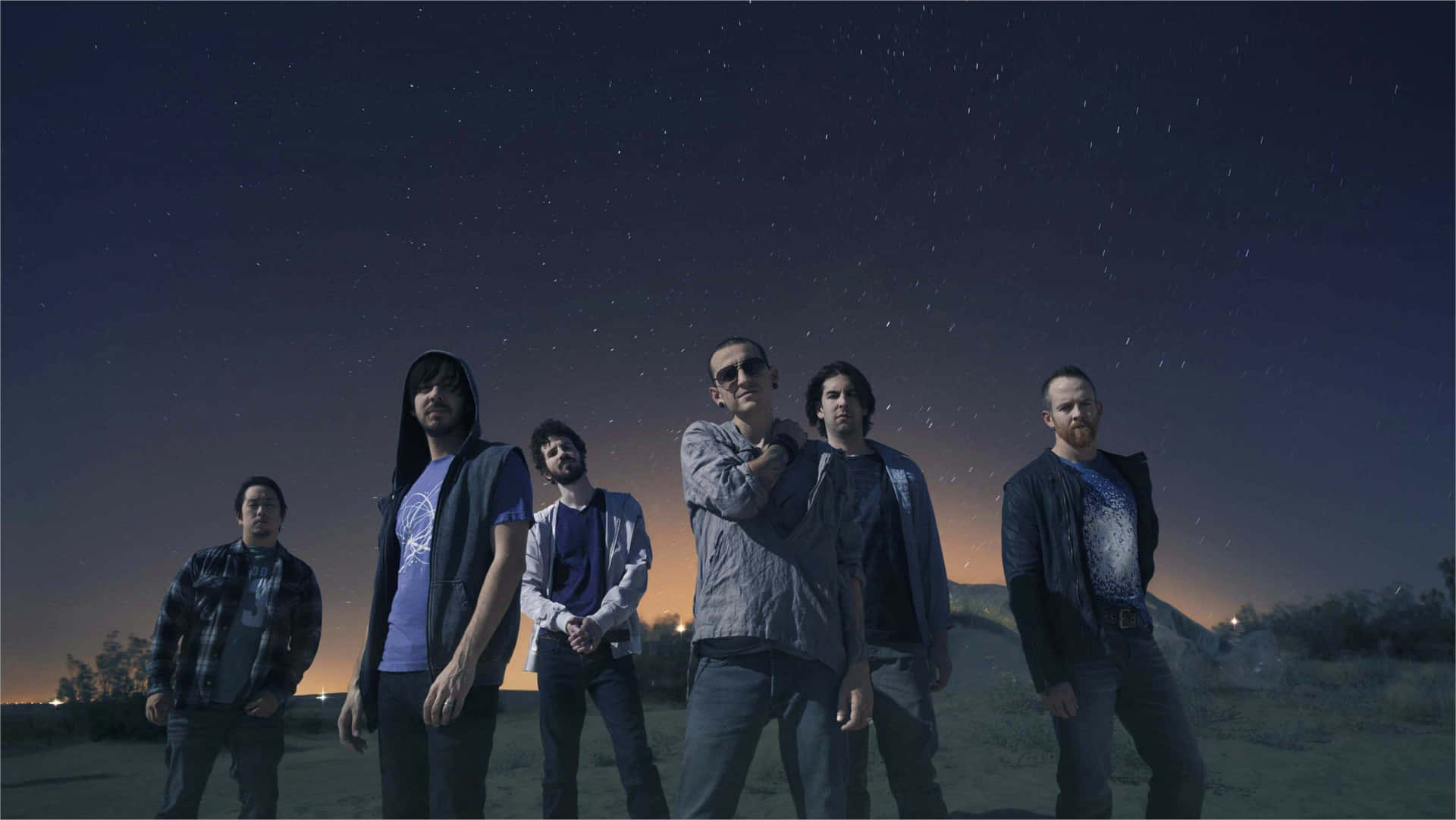 A Group Of Men Standing In A Field With Stars In The Sky Background