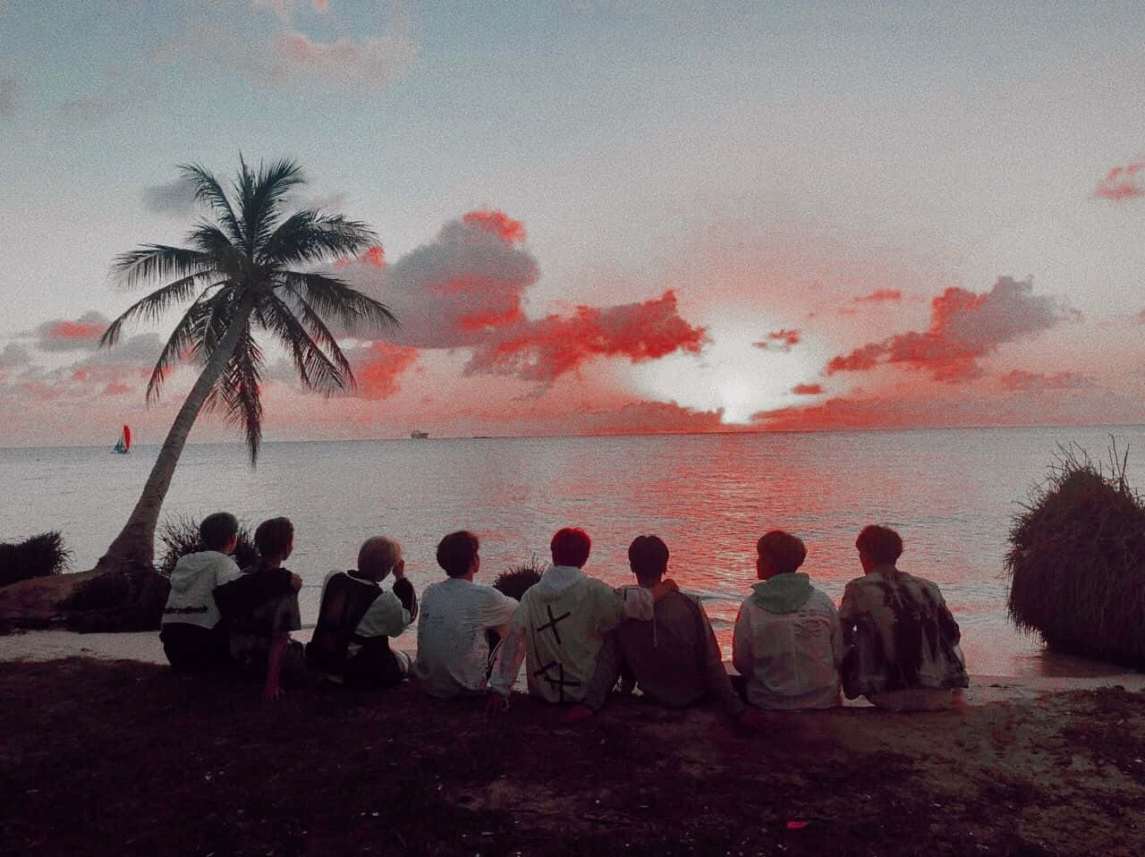 A Group Of People Sitting On The Beach Watching The Sunset Background