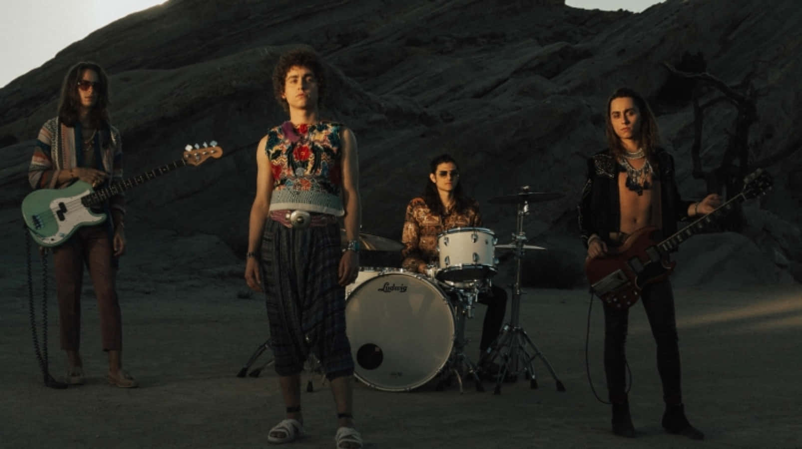 A Group Of People Standing In Front Of Rocks With Guitars Background