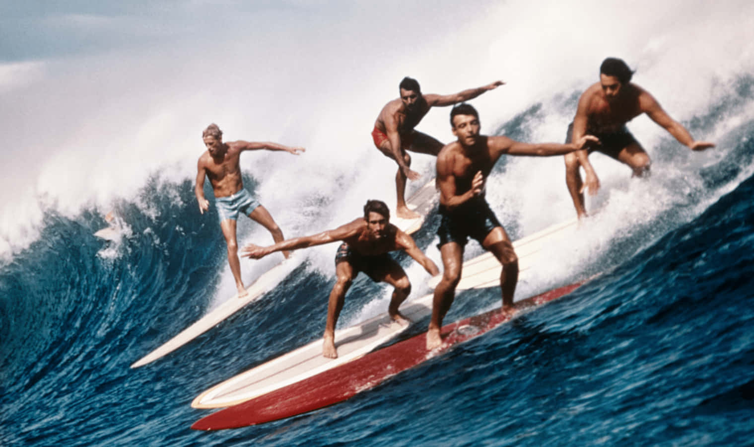A Group Of Surfers Riding A Wave On Surfboards