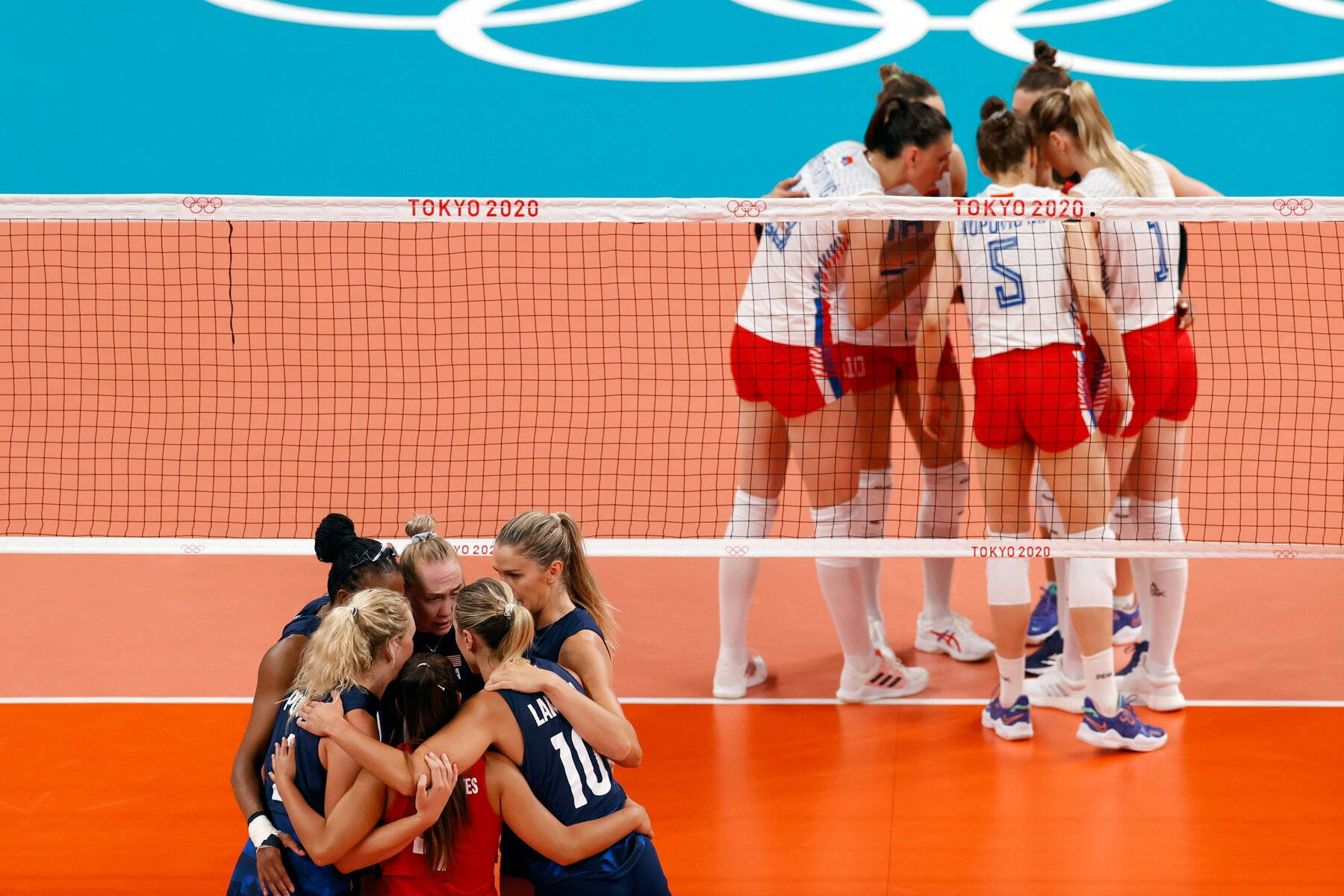 A Group Of Volleyball Players Huddle Around The Net Background