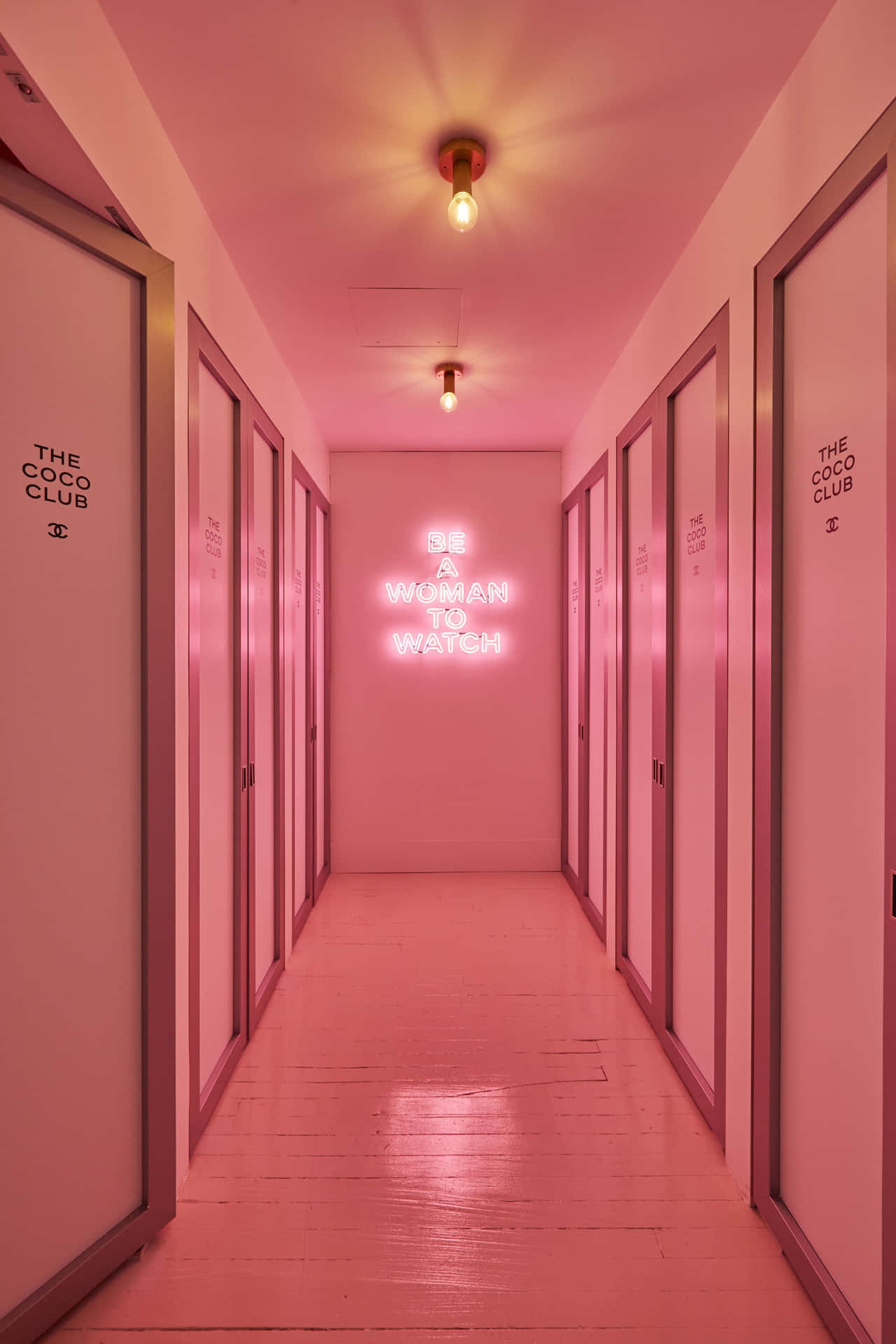 A Hallway With Pink Doors And A Neon Sign Background