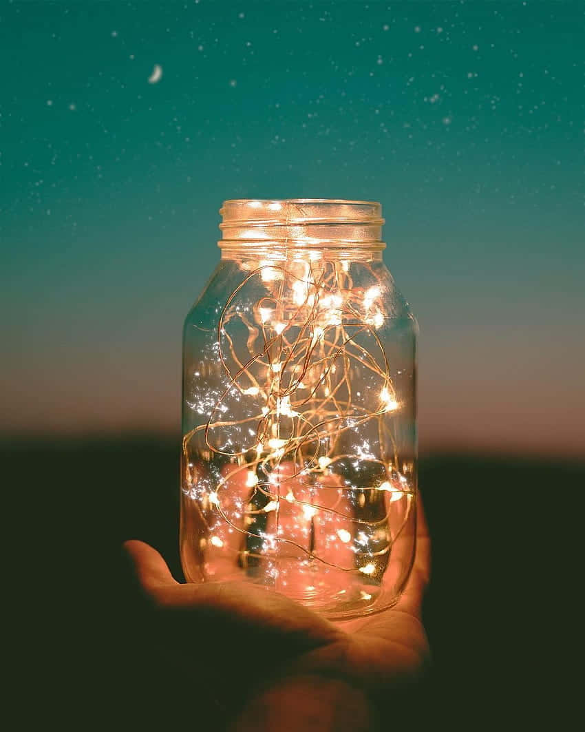 A Hand Holding A Jar Of Fairy Lights Background