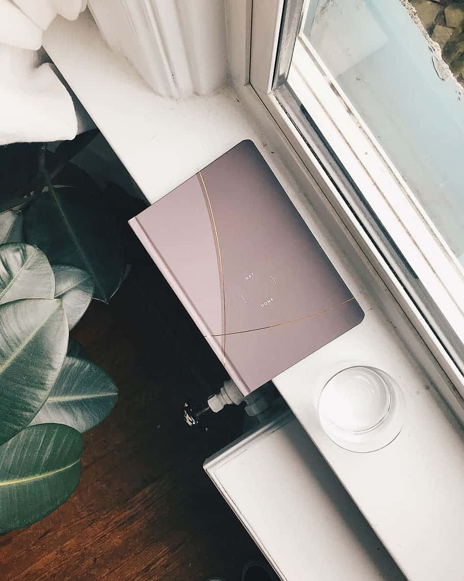 A Laptop On A Window Sill Next To A Plant Background