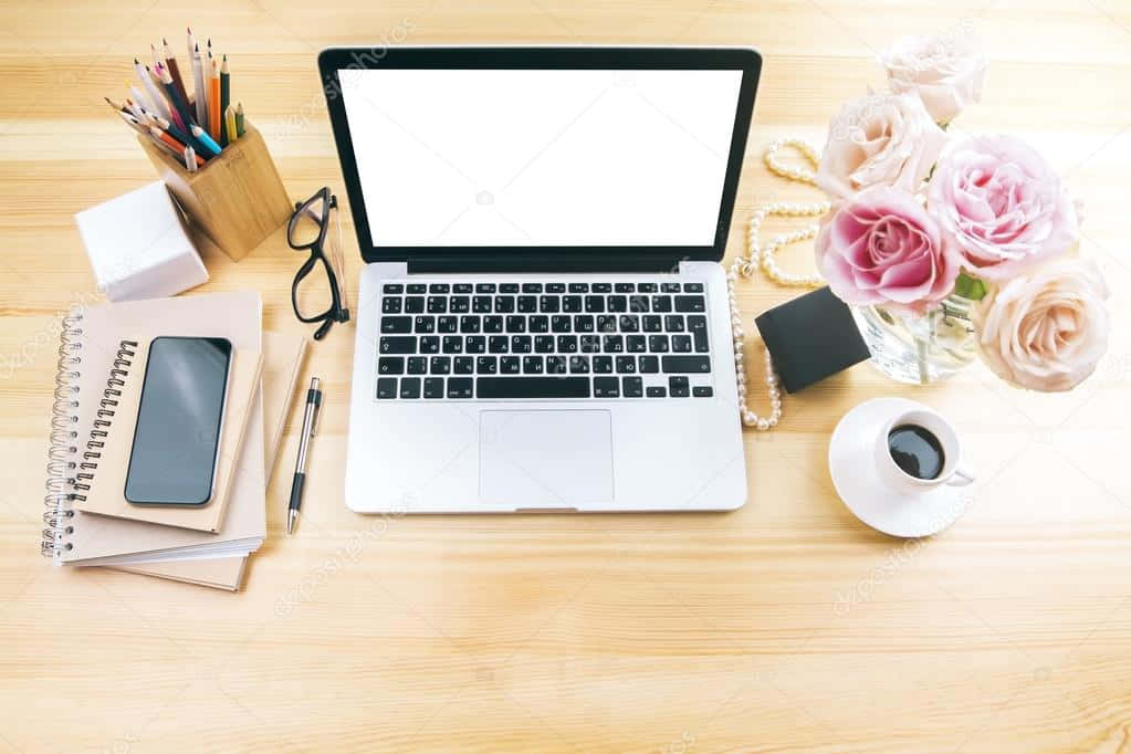 A Laptop, Phone, Flowers And Other Office Supplies On A Wooden Desk Background
