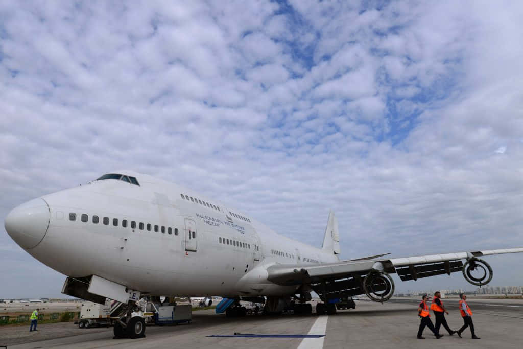 A Large Airplane On The Tarmac With People Walking Around It Background