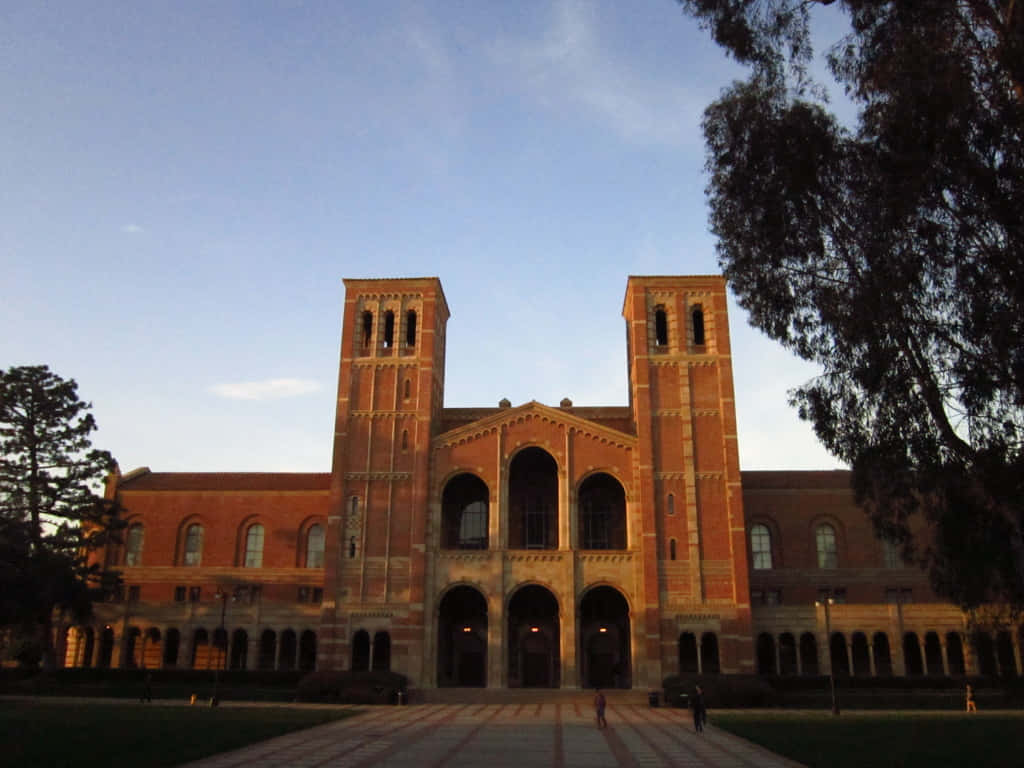 A Large Brick Building With Trees And A Clock Tower Background