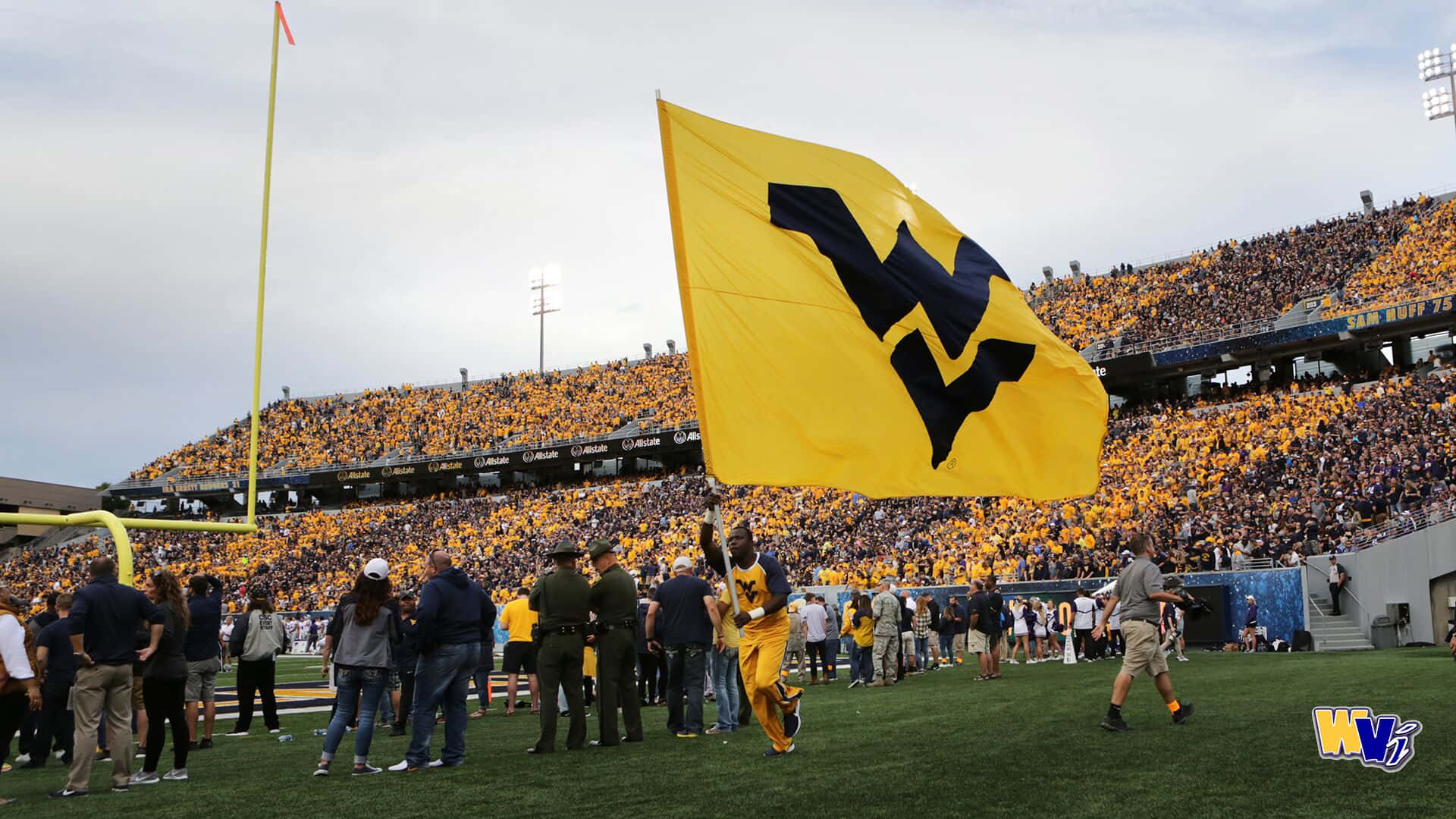 A Large Yellow Flag Is Held Up By A Crowd Of People Background