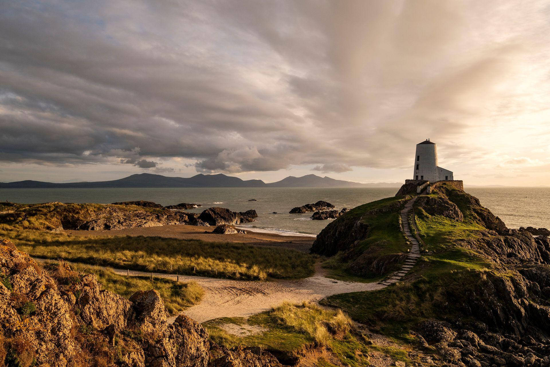 A Lighthouse Sits On Top Of A Rocky Cliff Overlooking The Ocean