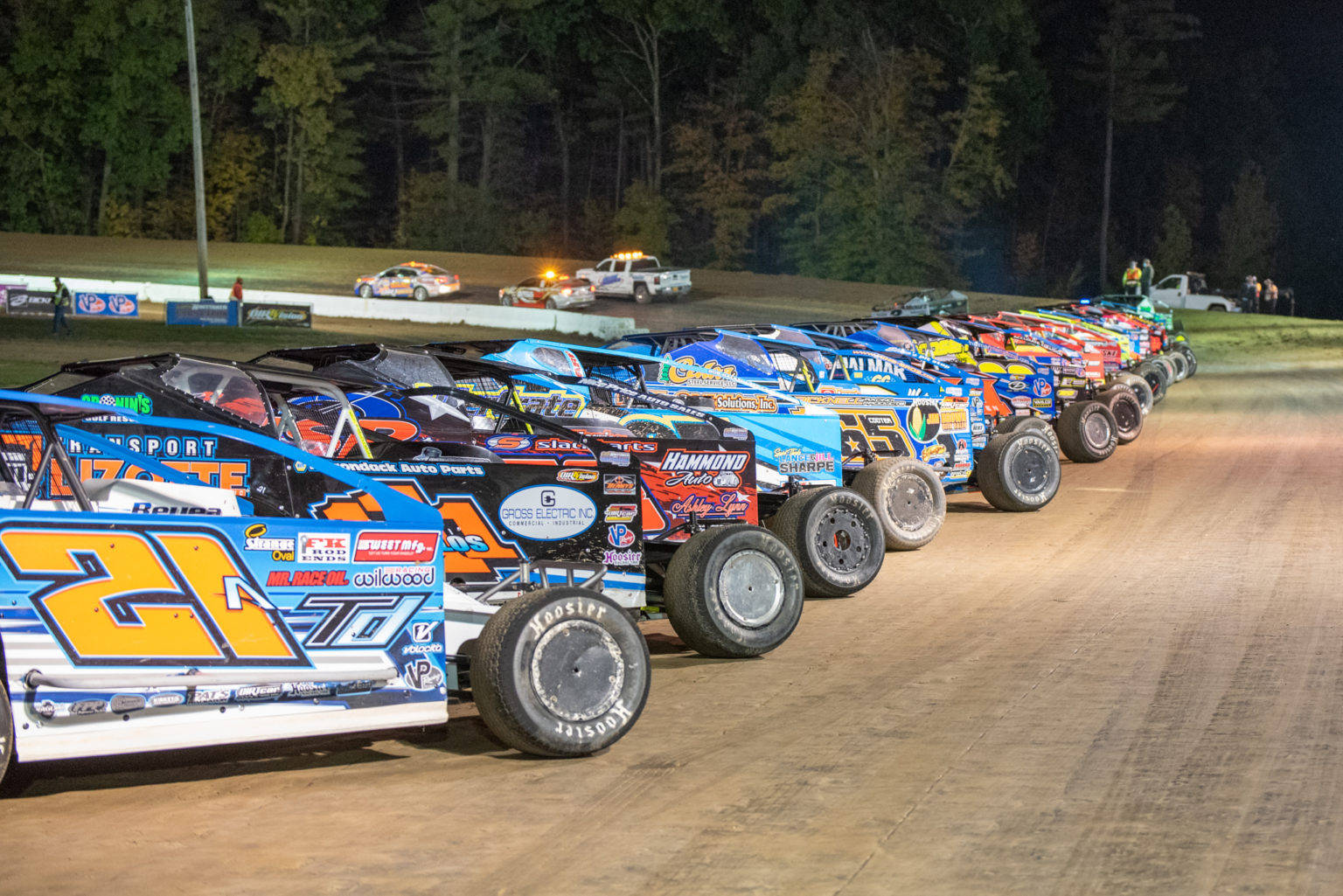 A Line Of Dirt Track Racing Cars At Night Background