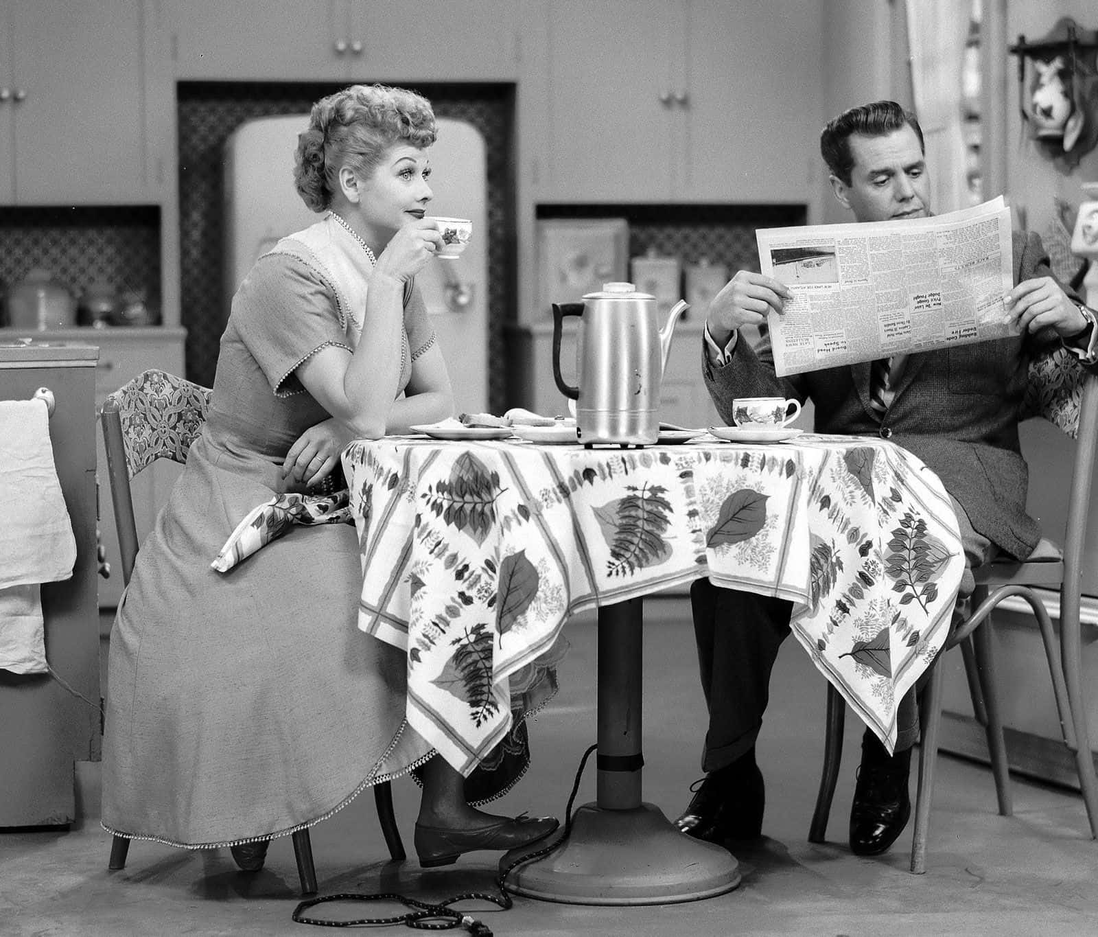 A Man And Woman Sitting At A Table Reading A Newspaper