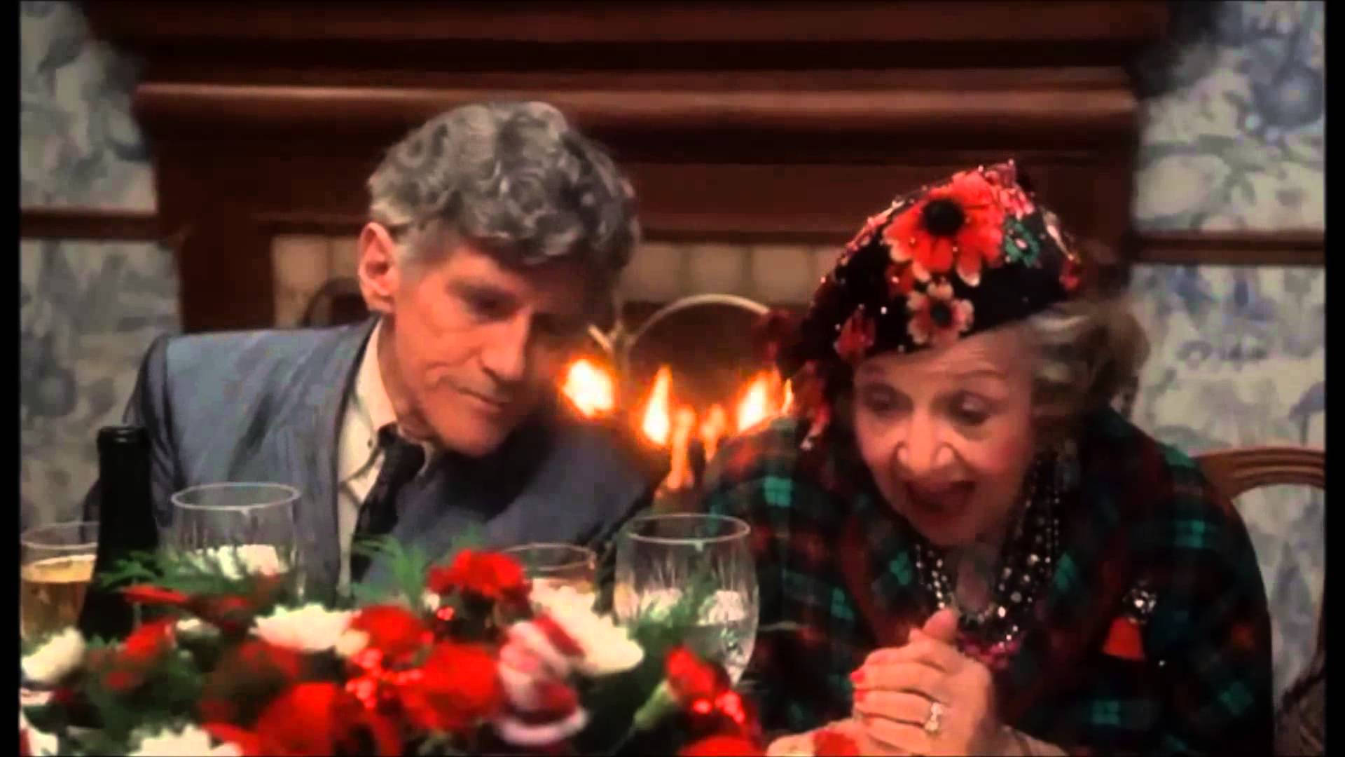 A Man And Woman Sitting At A Table With A Christmas Tree Background