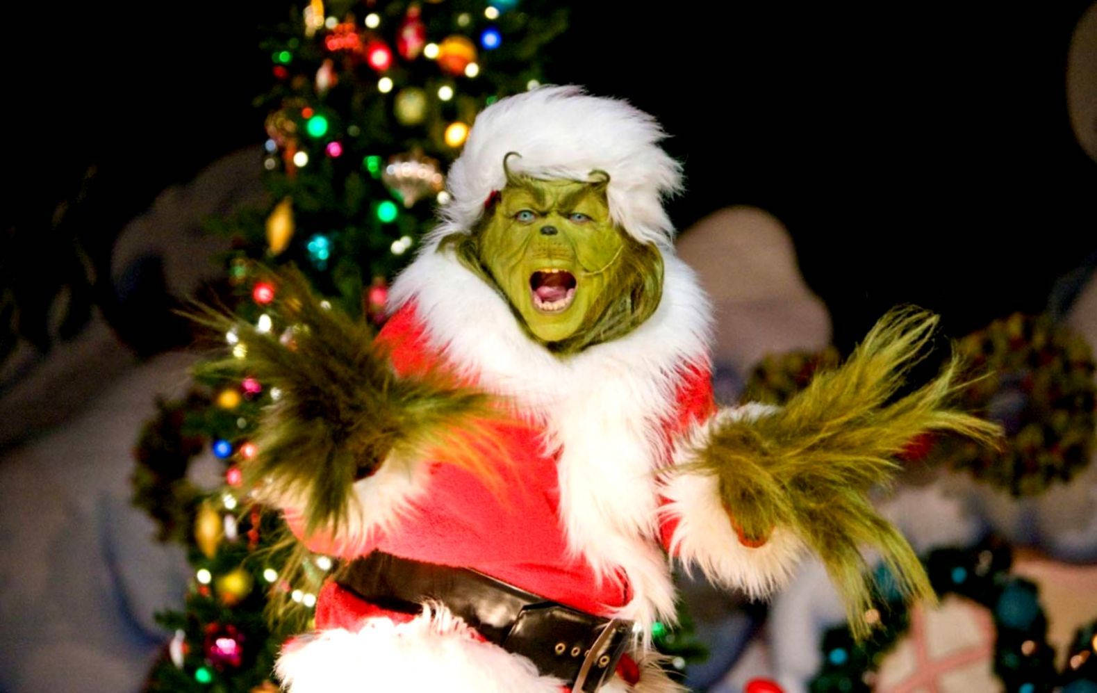 A Man Dressed As The Grinch Is Performing In Front Of A Christmas Tree Background