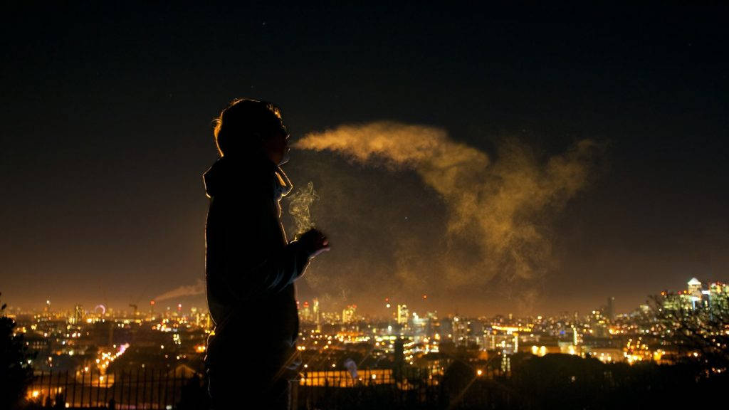 A Man Engaging In Solitary Reflection While Smoking Background