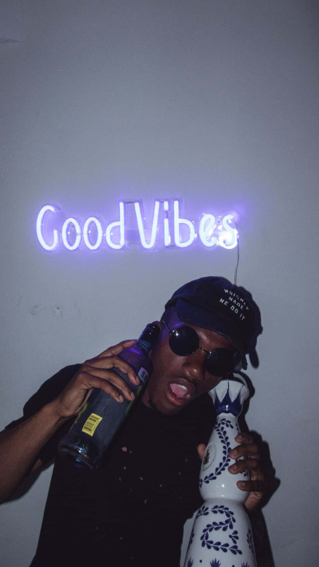 A Man Holding A Bottle Of Liquor And A Neon Sign That Says Good Vibes Background