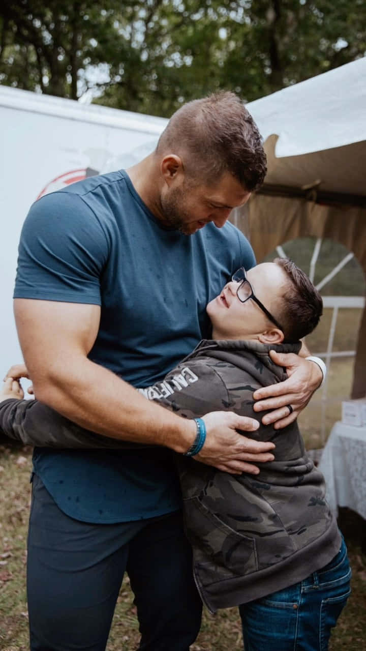 A Man Hugging A Young Boy In Front Of A Tent Background