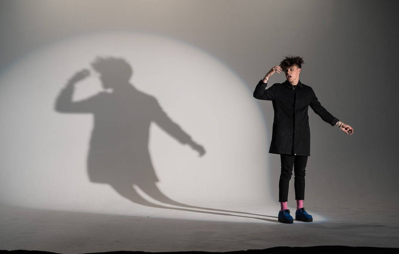 A Man In A Black Coat Standing In Front Of A Shadow Background