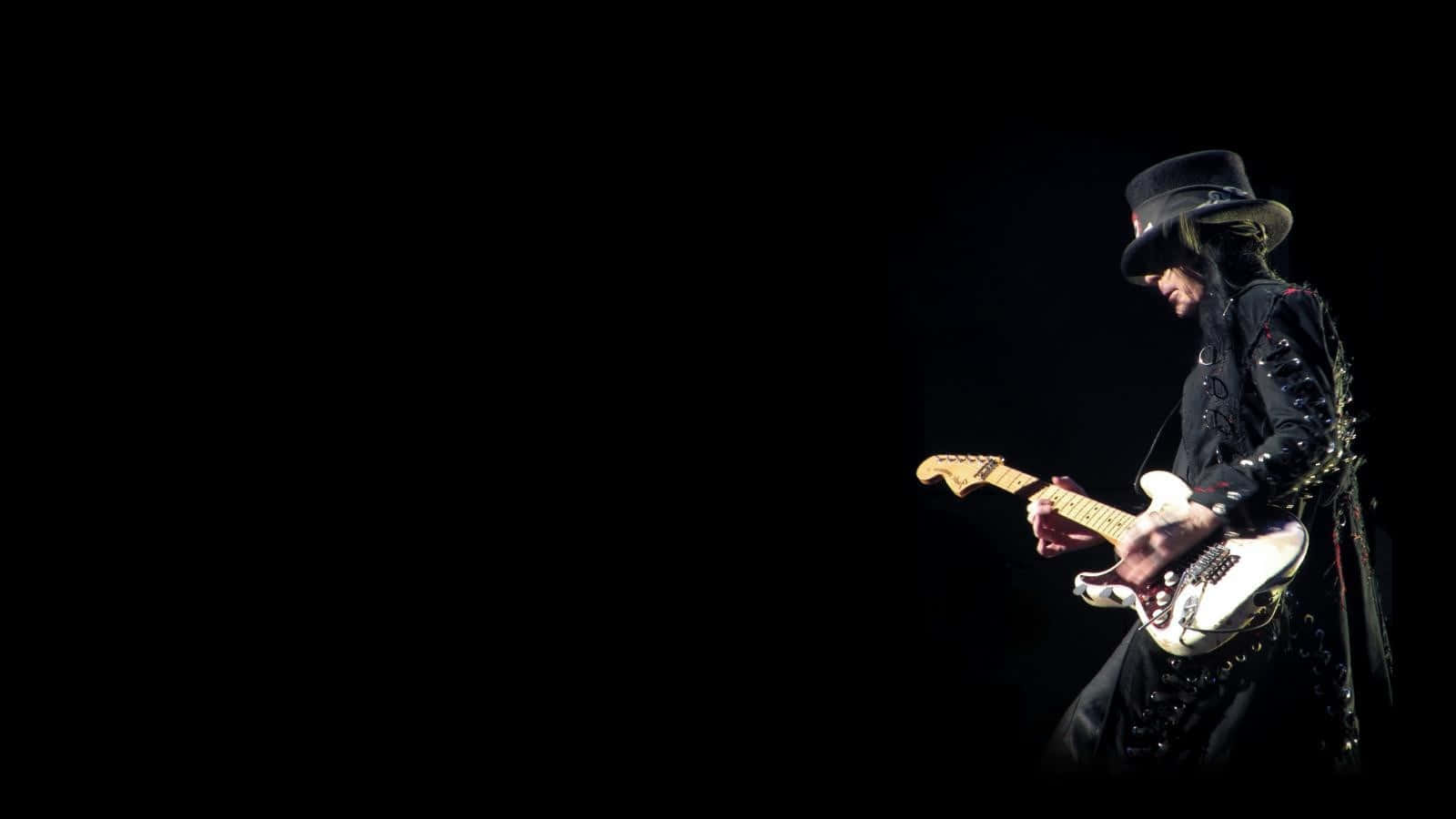 A Man In A Black Hat Playing An Electric Guitar Background